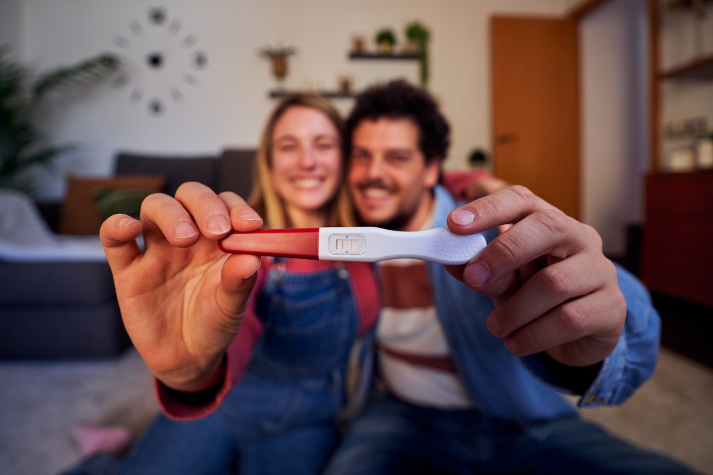 Joyful Caucasian couple happily showing a positive pregnancy test at home, announcing their future parenthood