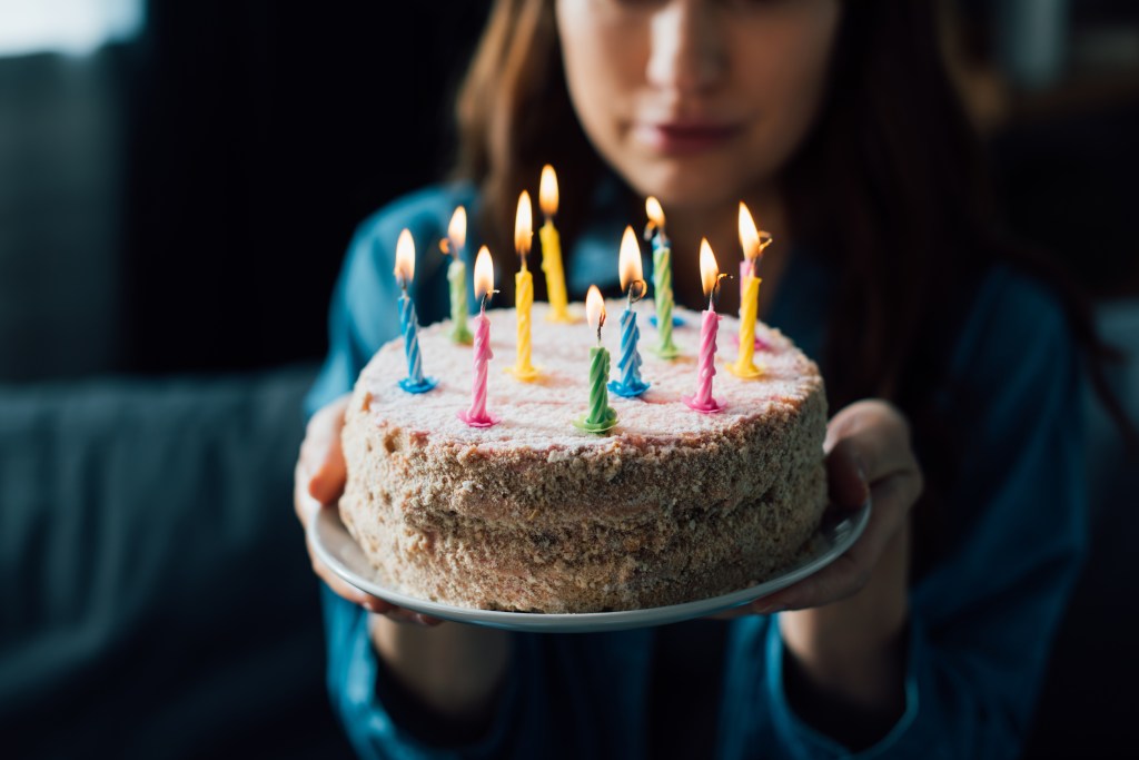 Sad woman holding a birthday cake with lit candles in selective focus