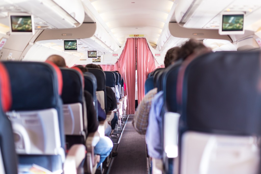 The interior of a commercial airliner filled with passengers, with a curtain separating economy and business class.